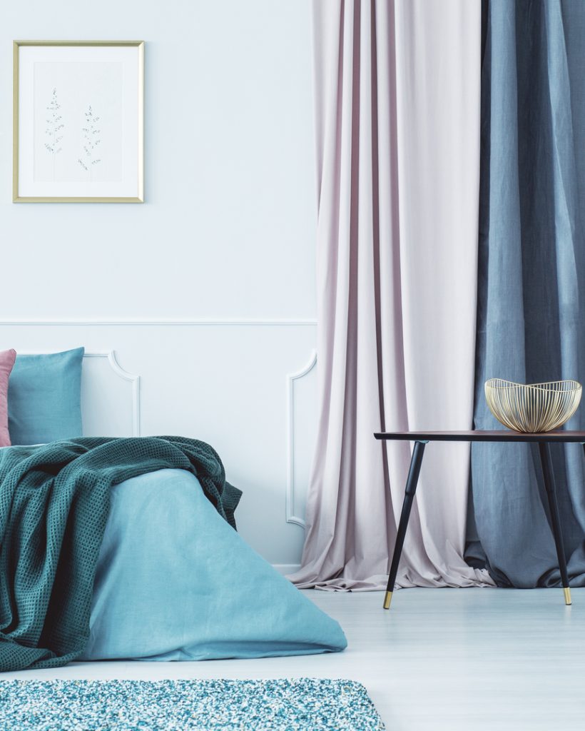 Two simple posters in gold frames hanging on the wall above double bed standing in bright interior with drapes