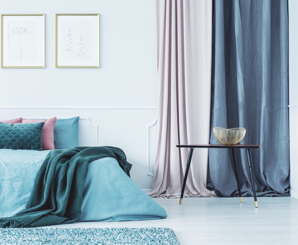 Two simple posters in gold frames hanging on the wall above double bed standing in bright interior with drapes